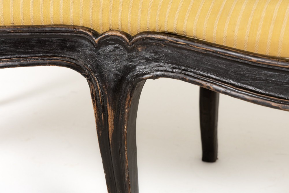 An 18th-century Italian ebonised sofa featuring a high serpentine backrest, mustard yellow striped upholstery, and carved cabriole legs. View V