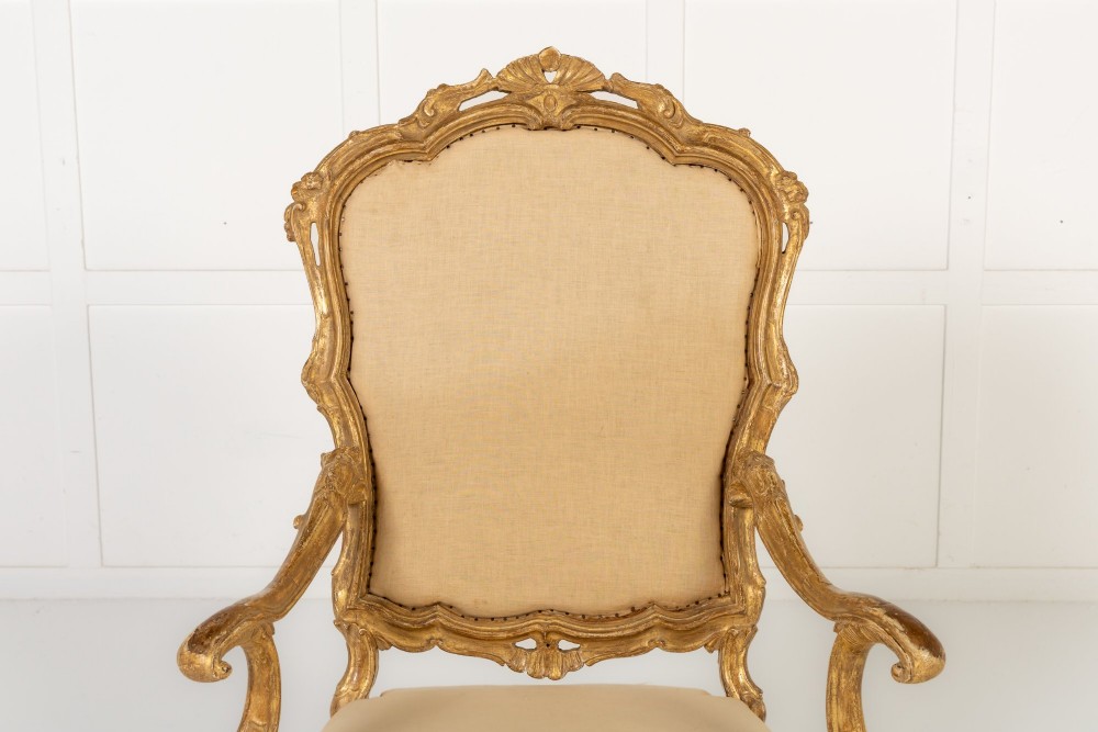 An 18th-century Italian carved giltwood armchair featuring neutral fabric upholstery, scrolled arms, and cabriole legs. View II