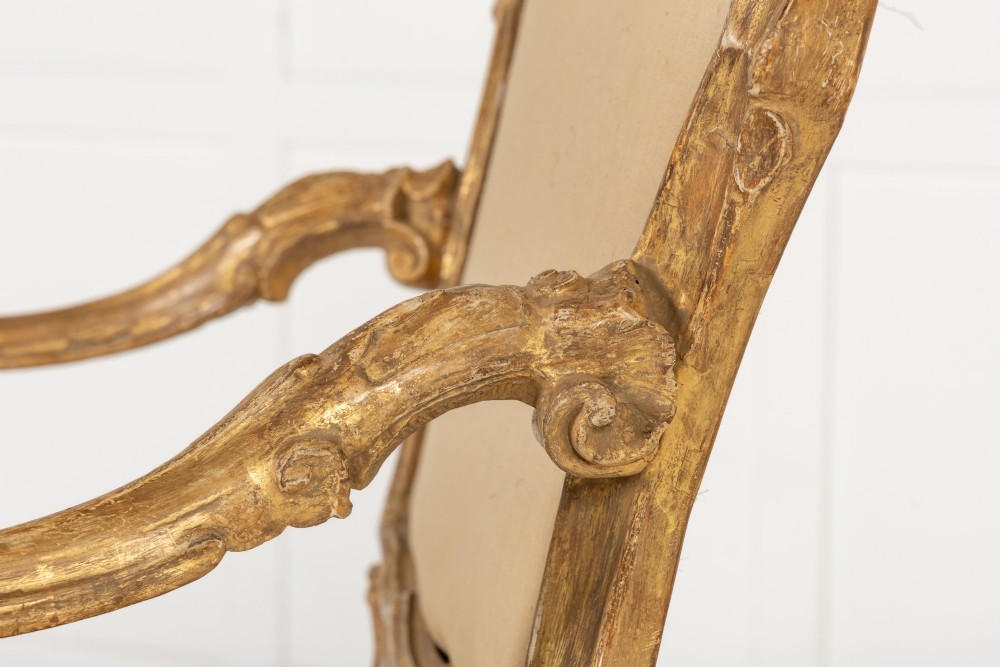 An 18th-century Italian carved giltwood armchair featuring neutral fabric upholstery, scrolled arms, and cabriole legs. View V