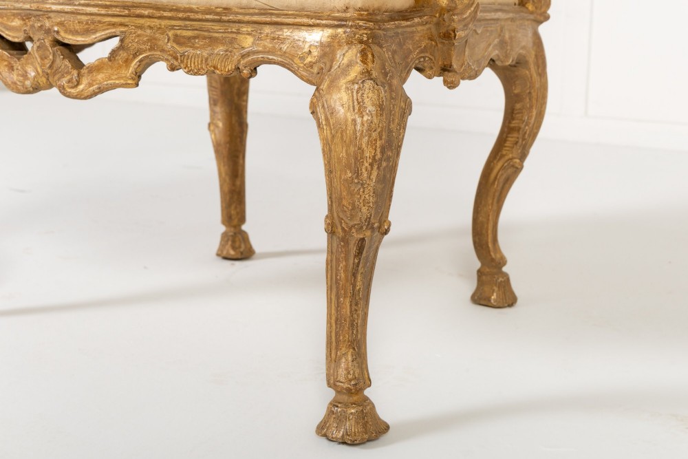 An 18th-century Italian carved giltwood armchair featuring neutral fabric upholstery, scrolled arms, and cabriole legs. View VII