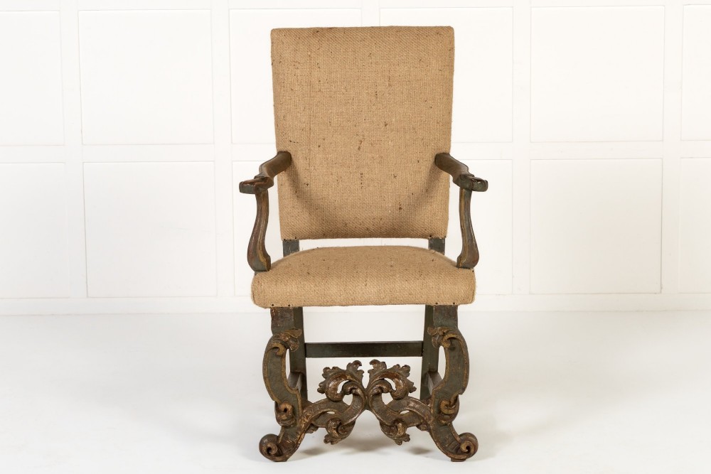 A high-backed 17th-century Italian Baroque armchair upholstered in beige hessian fabric with intricately carved wooden arms, legs, and a carved scroll front stretcher.