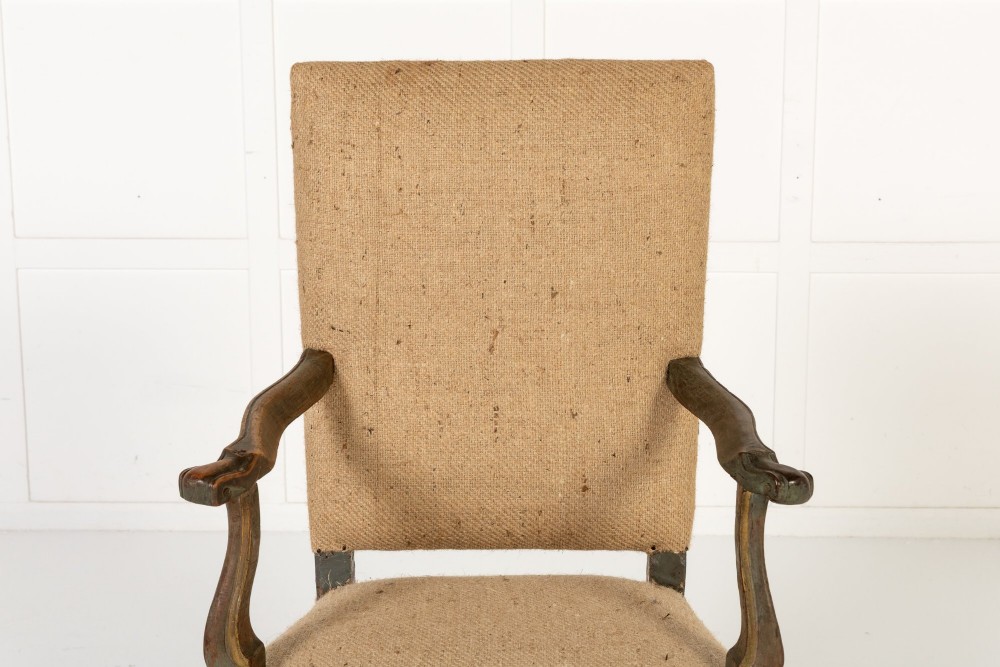 A high-backed 17th-century Italian Baroque armchair upholstered in beige hessian fabric with intricately carved wooden arms, legs, and a carved scroll front stretcher. View II