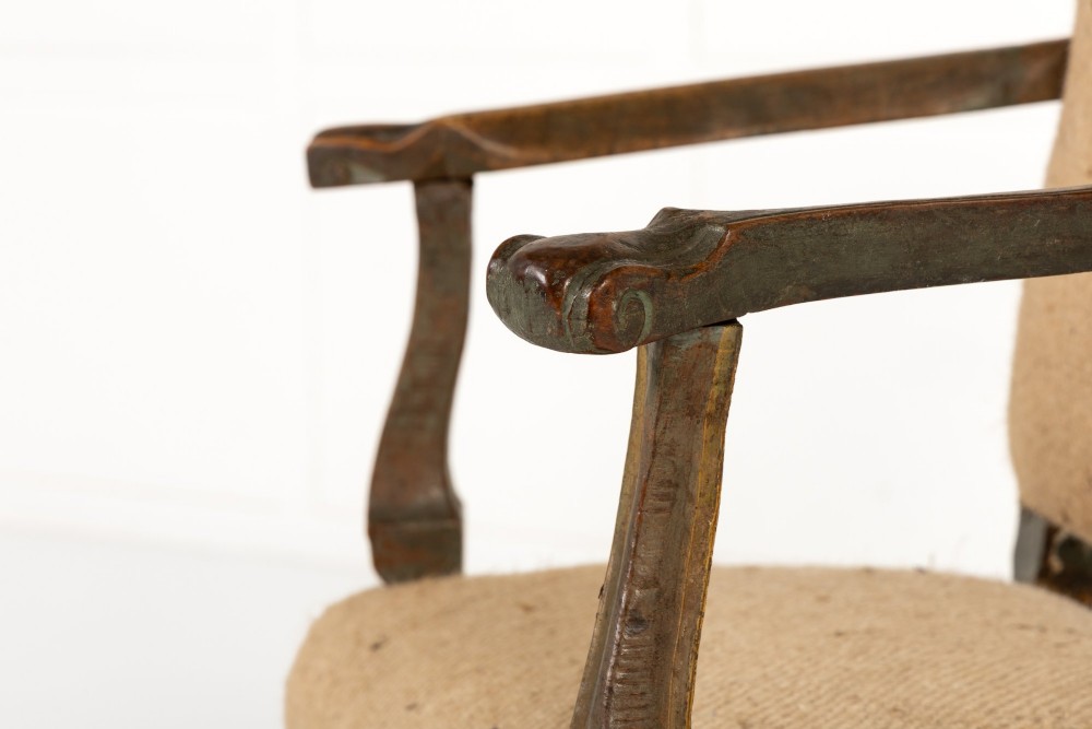 A high-backed 17th-century Italian Baroque armchair upholstered in beige hessian fabric with intricately carved wooden arms, legs, and a carved scroll front stretcher. View IV