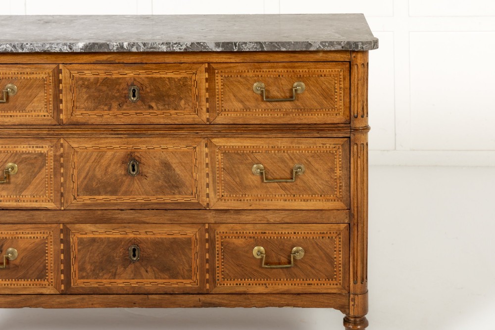 An 18th-century French walnut commode featuring three inlaid drawers, fluted corner pilasters, tapered legs, brass handles, and a grey marble top. View III
