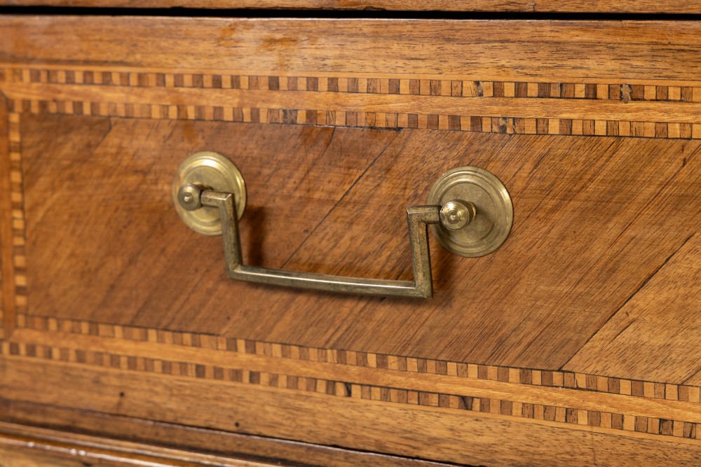 An 18th-century French walnut commode featuring three inlaid drawers, fluted corner pilasters, tapered legs, brass handles, and a grey marble top. View V