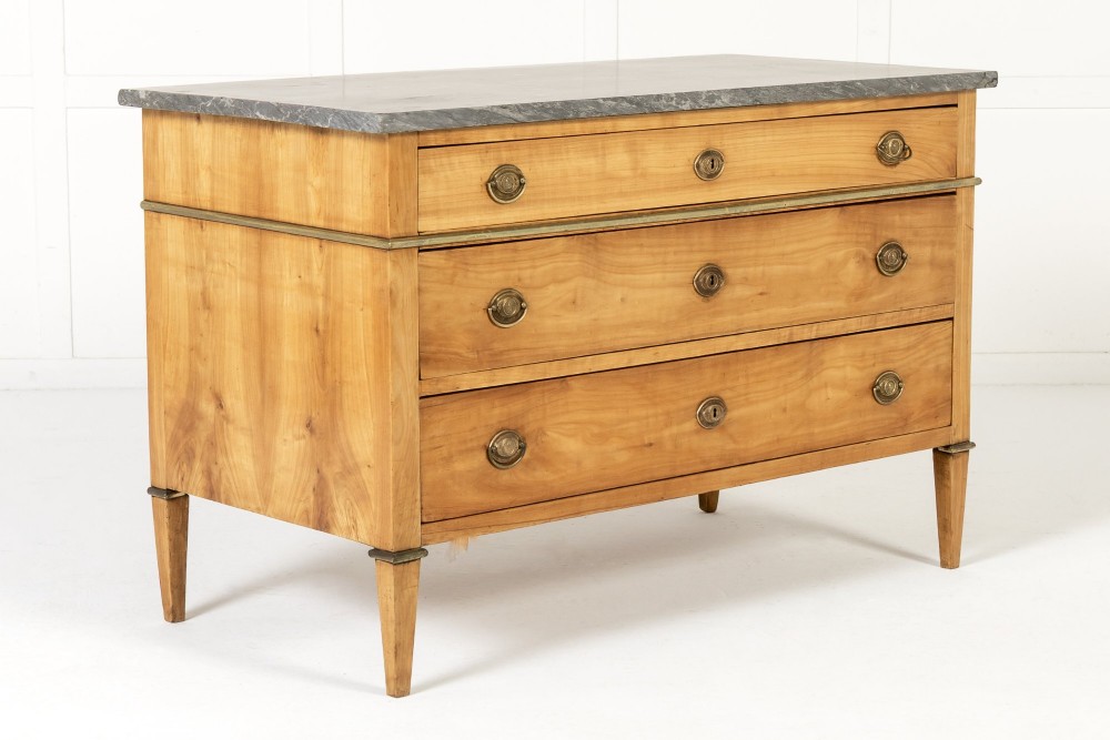 An 18th-century French cherrywood commode featuring three drawers with round brass ring pull handles, an oval keyhole escutcheon, tapered legs, and a grey marble top. View II