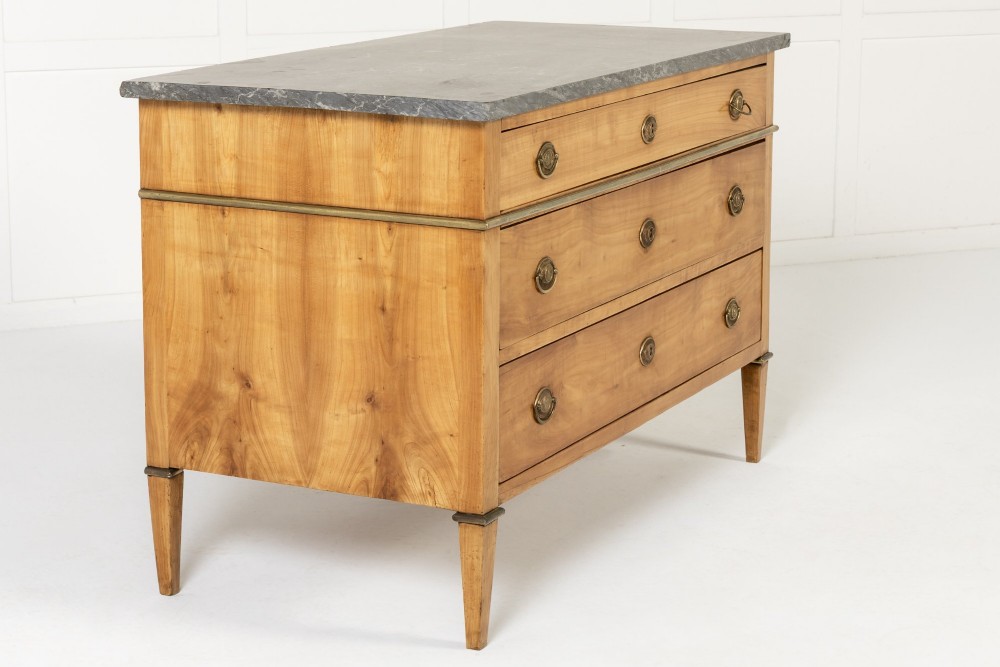 An 18th-century French cherrywood commode featuring three drawers with round brass ring pull handles, an oval keyhole escutcheon, tapered legs, and a grey marble top. View III