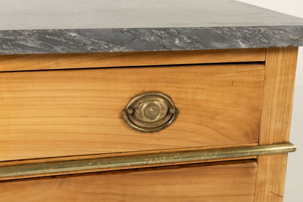 An 18th-century French cherrywood commode featuring three drawers with round brass ring pull handles, an oval keyhole escutcheon, tapered legs, and a grey marble top. View V