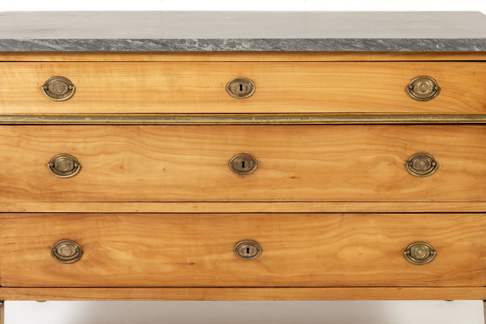 An 18th-century French cherrywood commode featuring three drawers with round brass ring pull handles, an oval keyhole escutcheon, tapered legs, and a grey marble top. View VI