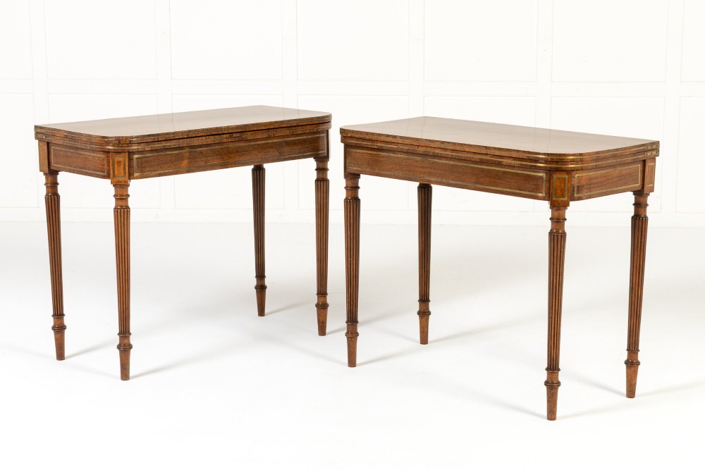 A pair of 19th-century English Regency rosewood foldover card tables with brass stringing inlay and fluted tapered legs.