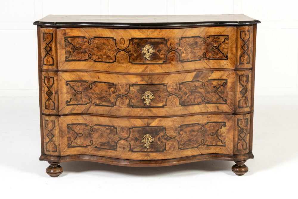 An 18th-century German walnut commode featuring three serpentine drawers with dark wood strapwork inlay and ornate brass escutcheons. View II