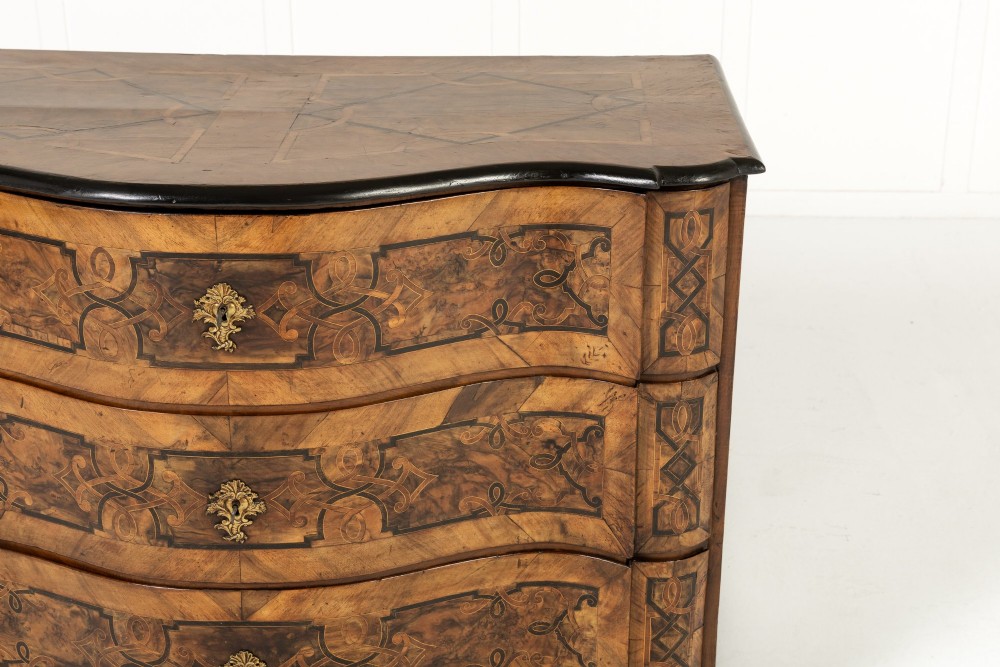 An 18th-century German walnut commode featuring three serpentine drawers with dark wood strapwork inlay and ornate brass escutcheons. View III