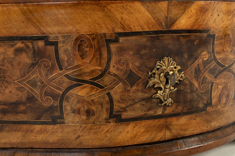 An 18th-century German walnut commode featuring three serpentine drawers with dark wood strapwork inlay and ornate brass escutcheons. View VI