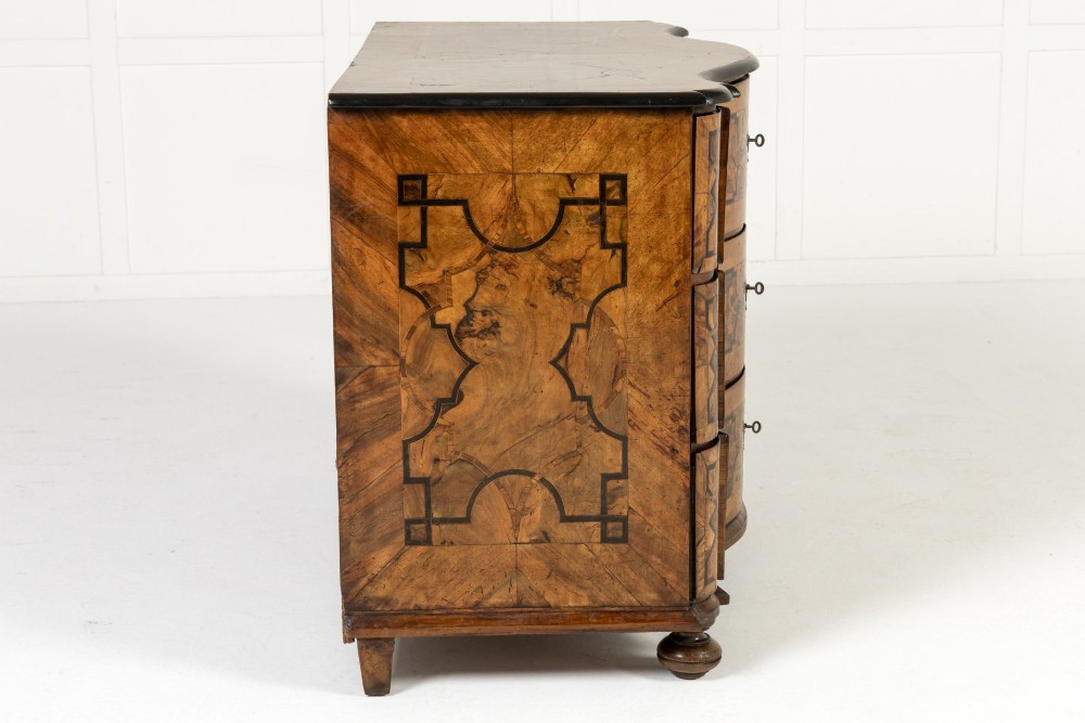 An 18th-century German walnut commode featuring three serpentine drawers with dark wood strapwork inlay and ornate brass escutcheons. View IX