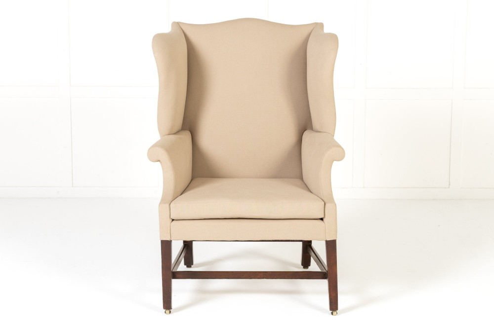 An 18th-century mahogany wingback armchair upholstered in neutral beige fabric with square timber legs and brass castors. View II