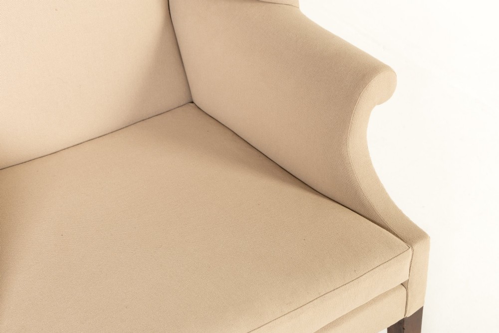 An 18th-century mahogany wingback armchair upholstered in neutral beige fabric with square timber legs and brass castors. View III