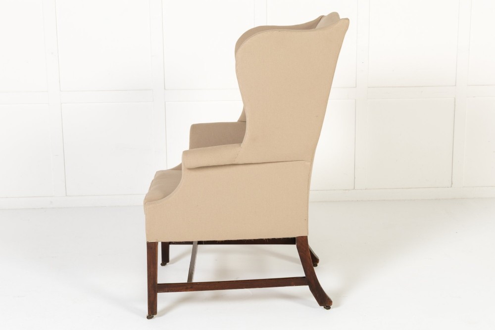 An 18th-century mahogany wingback armchair upholstered in neutral beige fabric with square timber legs and brass castors. View VI