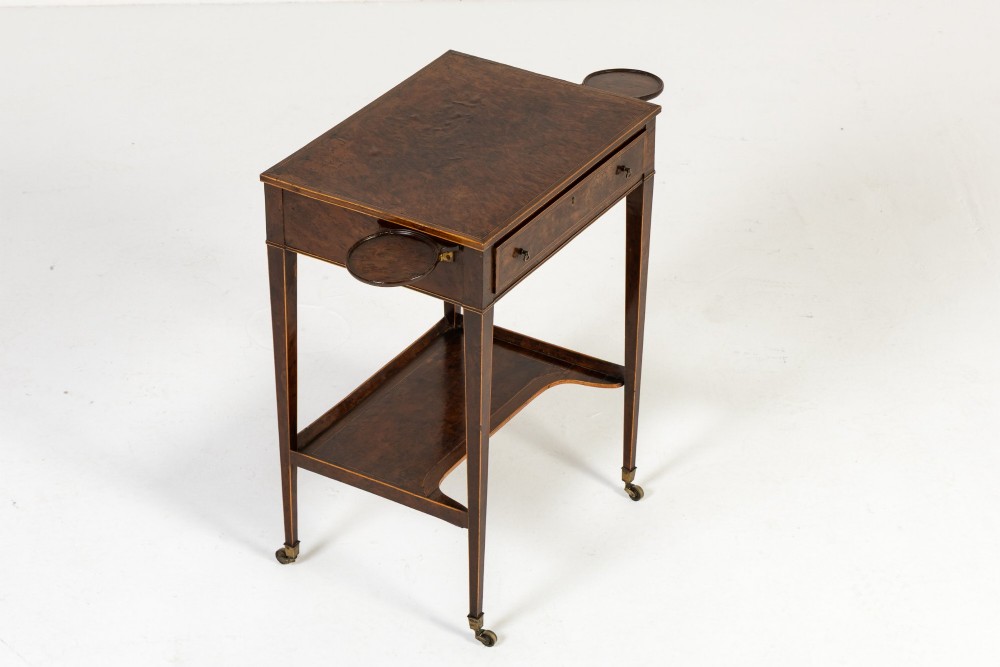 A small 19th-century burr yew wood writing table featuring a single drawer, two pull-out side slides, a lower undershelf, inlaid stringing, tapered legs, and brass casters.