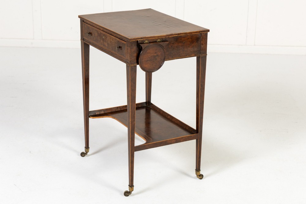 A small 19th-century burr yew wood writing table featuring a single drawer, two pull-out side slides, a lower undershelf, inlaid stringing, tapered legs, and brass casters. View VII