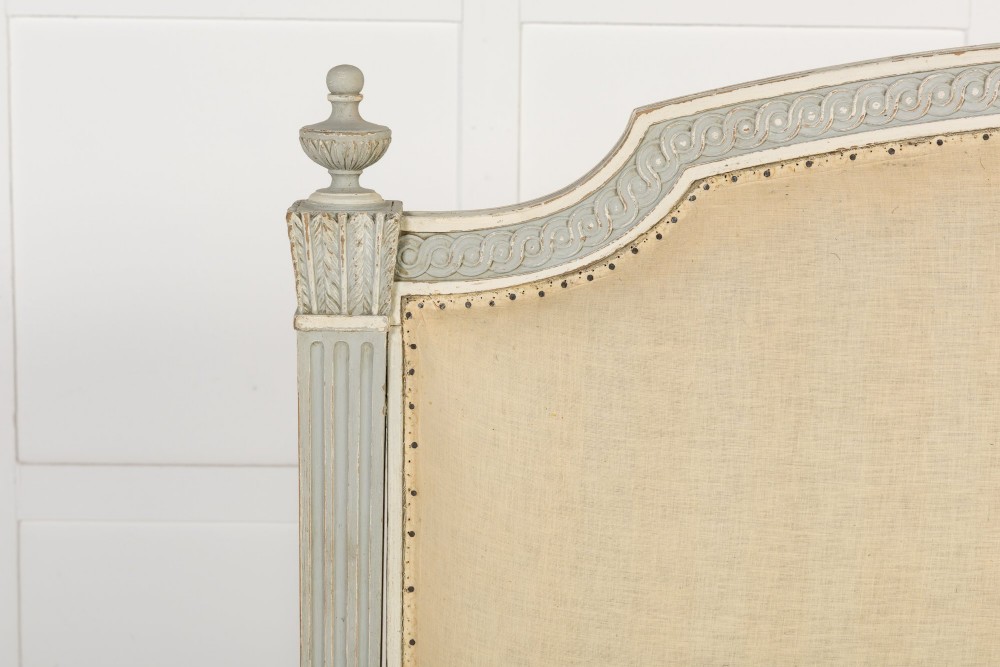 A 19th-century French Neoclassical double bed frame with a light grey painted finish, fluted posts topped with finials, and an arched cream upholstered headboard. View II