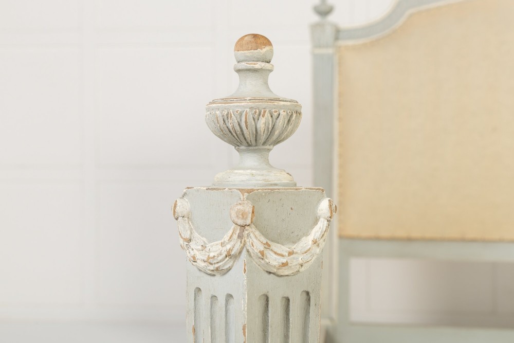 A 19th-century French Neoclassical double bed frame with a light grey painted finish, fluted posts topped with finials, and an arched cream upholstered headboard. View V