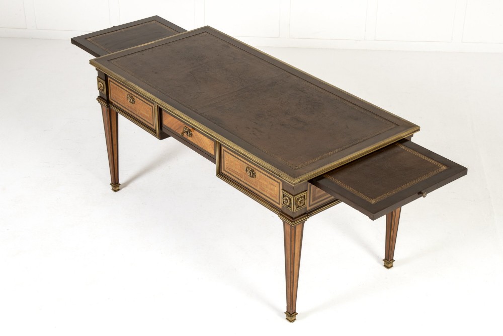 A 19th-century French Louis XVI style bureau plat writing desk featuring geometric parquetry inlay, three frieze drawers, a leather top insert, and brass mounts on square tapered legs. View X