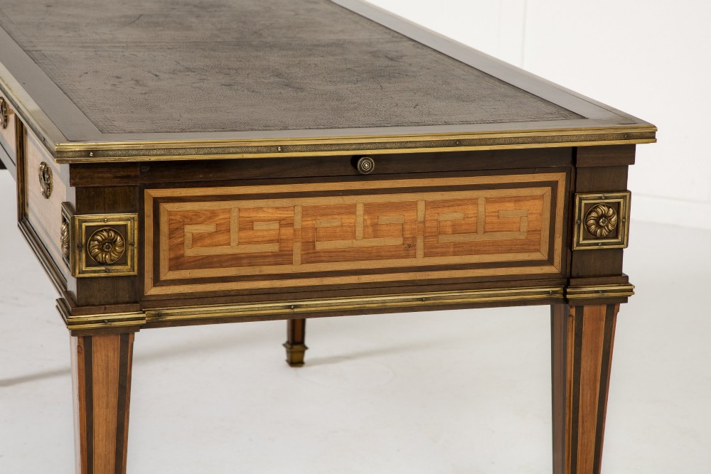 A 19th-century French Louis XVI style bureau plat writing desk featuring geometric parquetry inlay, three frieze drawers, a leather top insert, and brass mounts on square tapered legs. View XI