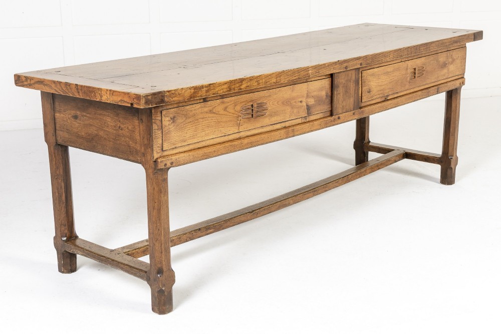 A long, rectangular 18th-century French oak table featuring two drawers with carved recessed pulls and lower stretchers connecting the legs.