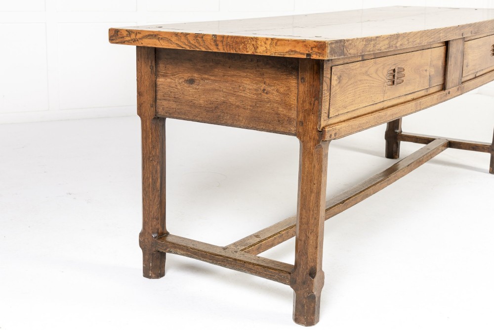 A long, rectangular 18th-century French oak table featuring two drawers with carved recessed pulls and lower stretchers connecting the legs. View X