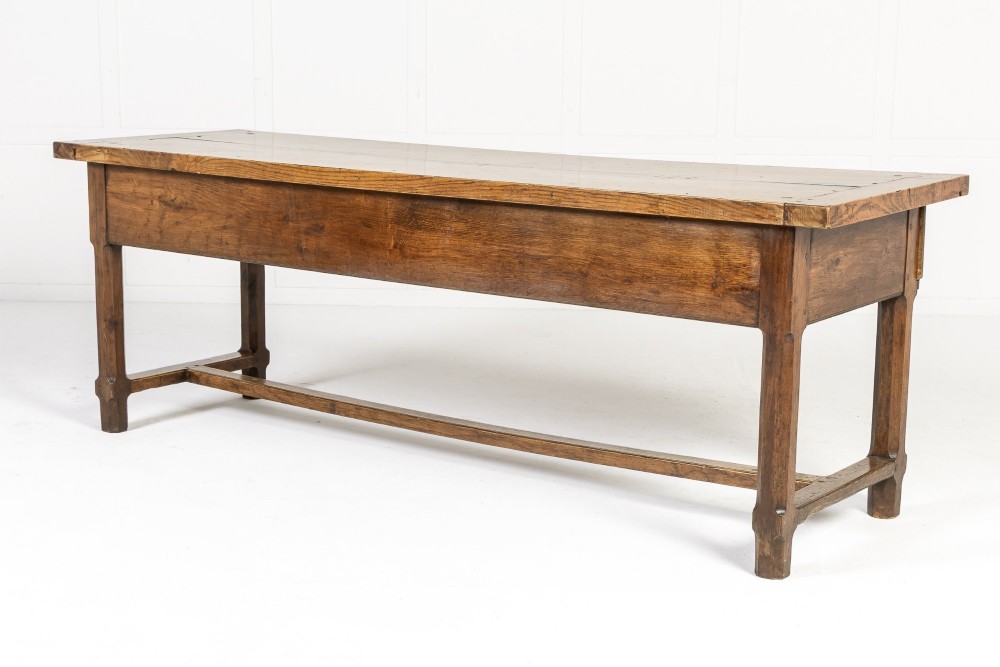 A long, rectangular 18th-century French oak table featuring two drawers with carved recessed pulls and lower stretchers connecting the legs. View XII