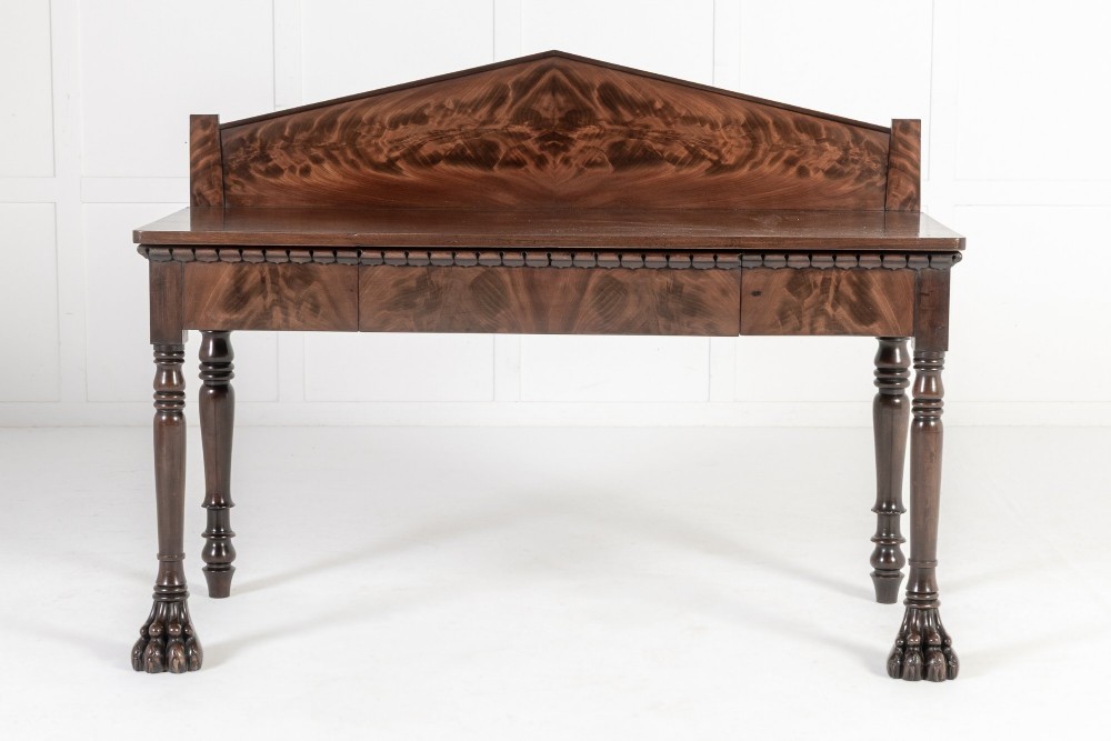 A 19th-century Regency mahogany serving table featuring a pointed splashback upstand, decorative carved frieze, turned front legs, and carved lion paw feet. View II