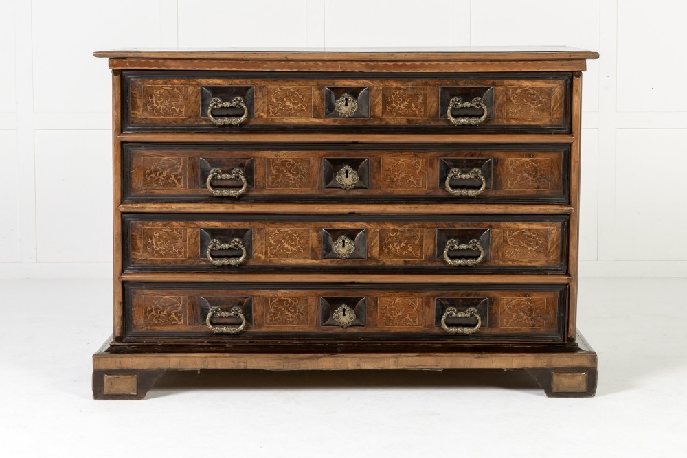 An 18th-century Italian walnut chest of drawers featuring foliage marquetry, brass drop handles, and geometric side moulding.