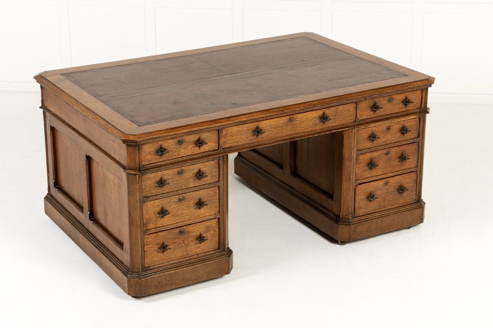 A large 19th-century English oak partners desk with twin pedestals, multiple drawers, metal drop handles, and panelled sides.