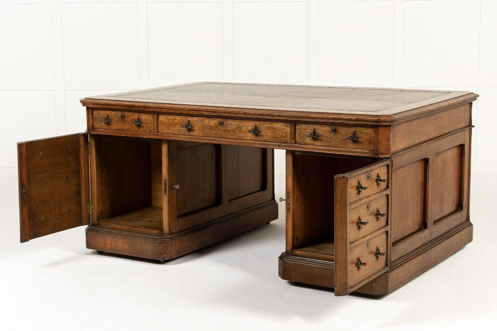 A large 19th-century English oak partners desk with twin pedestals, multiple drawers, metal drop handles, and panelled sides. View X