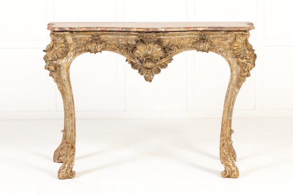 An 18th-century Italian Rococo console table featuring carved silver gilt legs with central shell motifs and a contoured variegated marble top.
