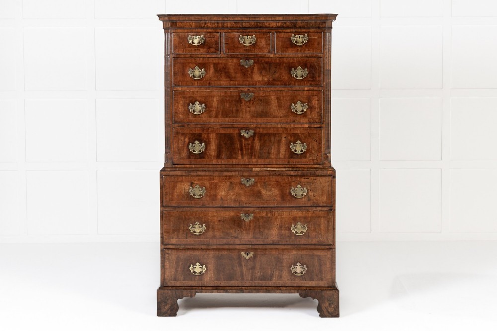 An 18th-century English walnut chest on chest featuring stacked drawers, figured timber veneers, brass backplate handles, and bracket feet.