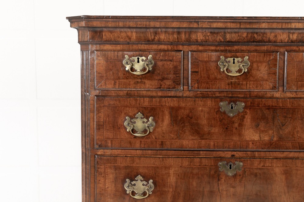 An 18th-century English walnut chest on chest featuring stacked drawers, figured timber veneers, brass backplate handles, and bracket feet. View V