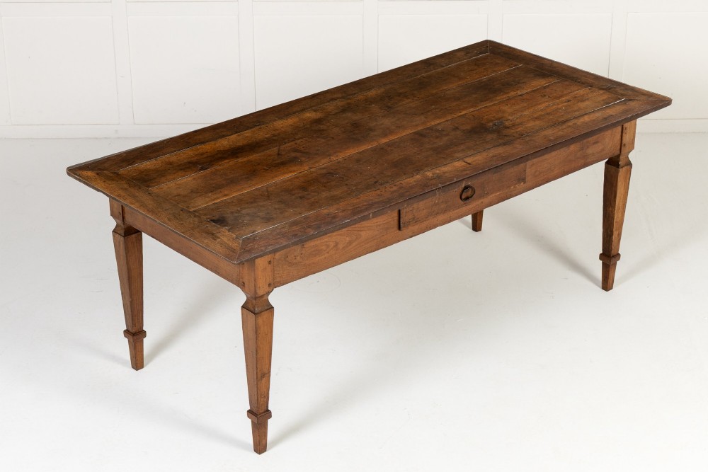 An 18th-century French cherrywood rectangular farmhouse dining table featuring a framed plank top, frieze drawer, and tapered legs.