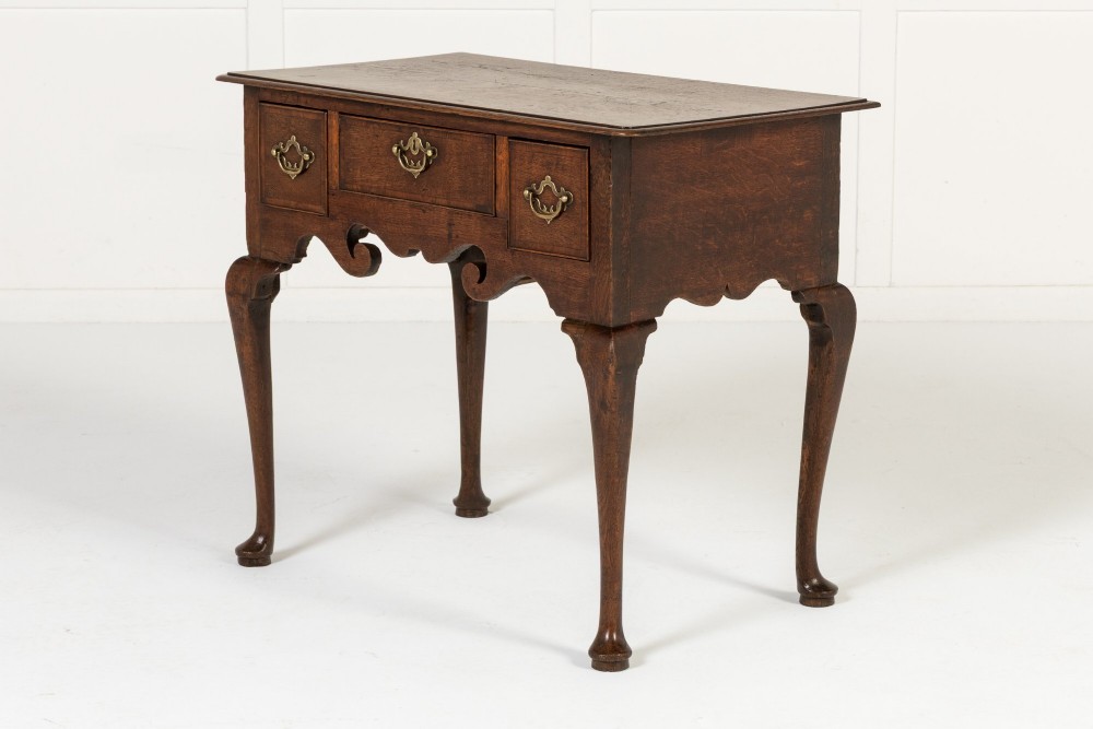 An 18th-century dark oak lowboy table featuring three drawers with brass handles, a shaped apron, and cabriole legs terminating in pad feet. View II