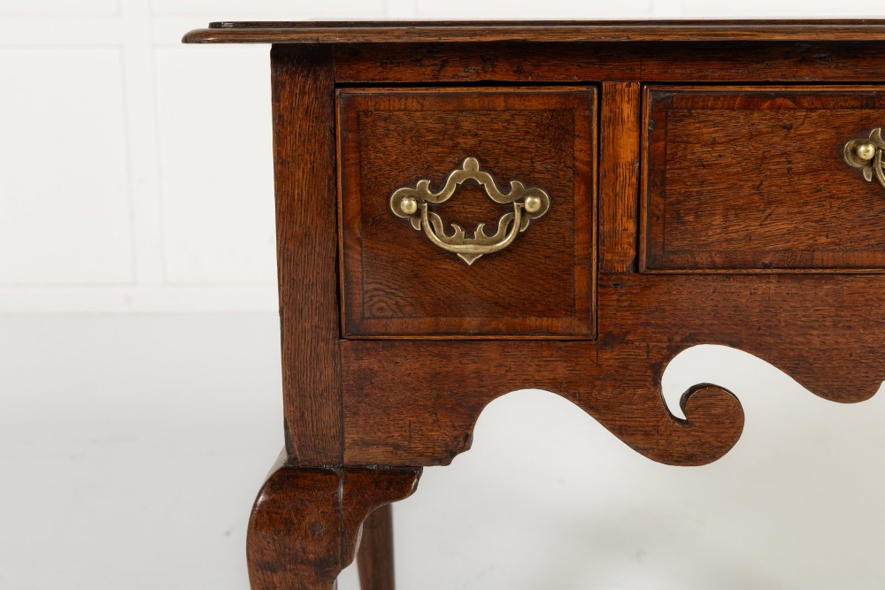 An 18th-century dark oak lowboy table featuring three drawers with brass handles, a shaped apron, and cabriole legs terminating in pad feet. View IV