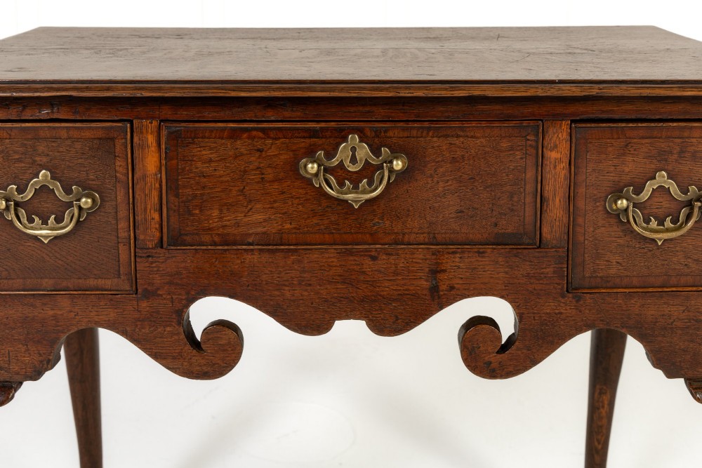 An 18th-century dark oak lowboy table featuring three drawers with brass handles, a shaped apron, and cabriole legs terminating in pad feet. View V