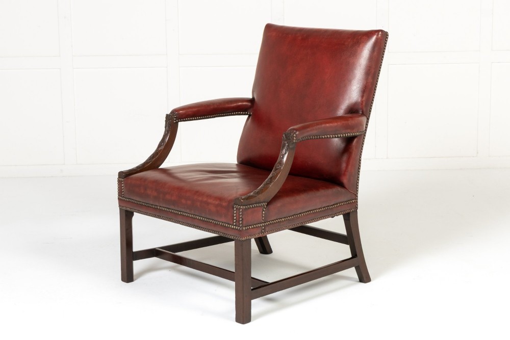 An 18th-century English Gainsborough armchair featuring deep red leather upholstery with brass studding, carved mahogany arms, and square legs.