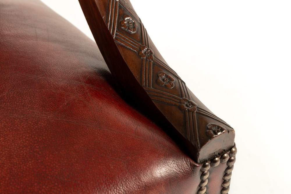 An 18th-century English Gainsborough armchair featuring deep red leather upholstery with brass studding, carved mahogany arms, and square legs. View V