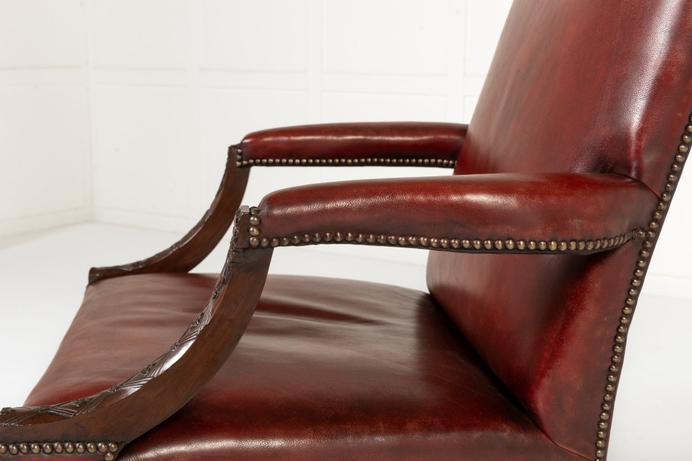 An 18th-century English Gainsborough armchair featuring deep red leather upholstery with brass studding, carved mahogany arms, and square legs. View VI