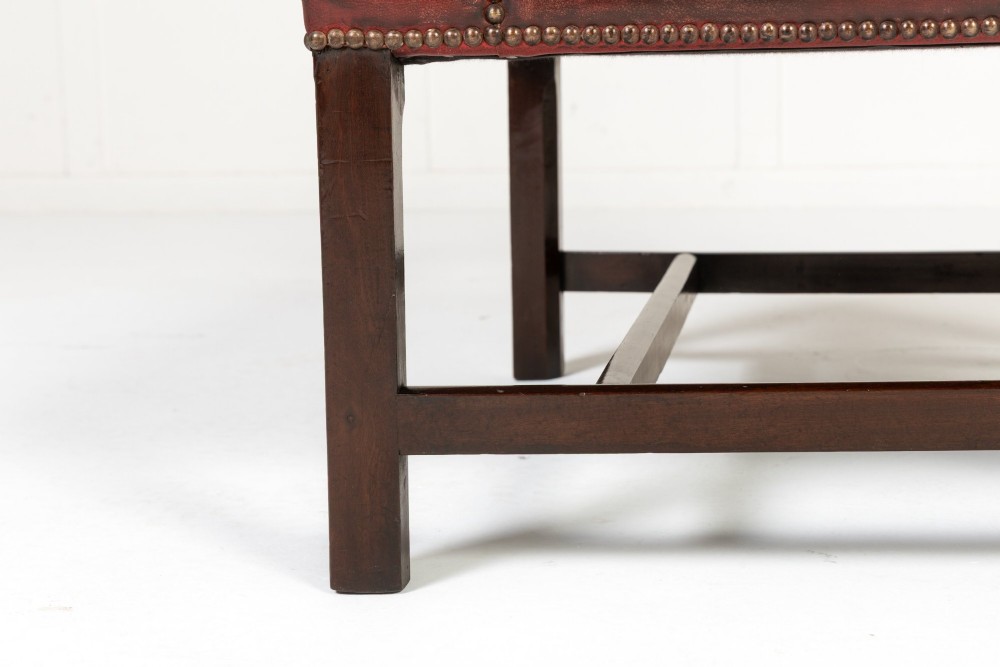 An 18th-century English Gainsborough armchair featuring deep red leather upholstery with brass studding, carved mahogany arms, and square legs. View VIII