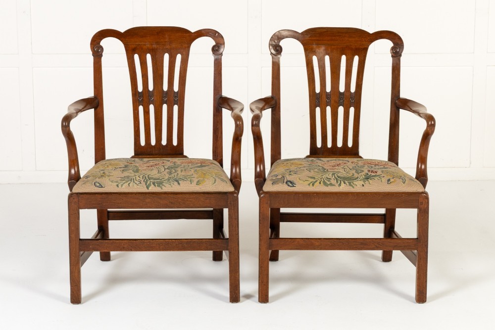 A pair of 18th-century George III mahogany armchairs featuring carved crest rails, vertical slatted splats, curved armrests, and needlepoint upholstered seats.