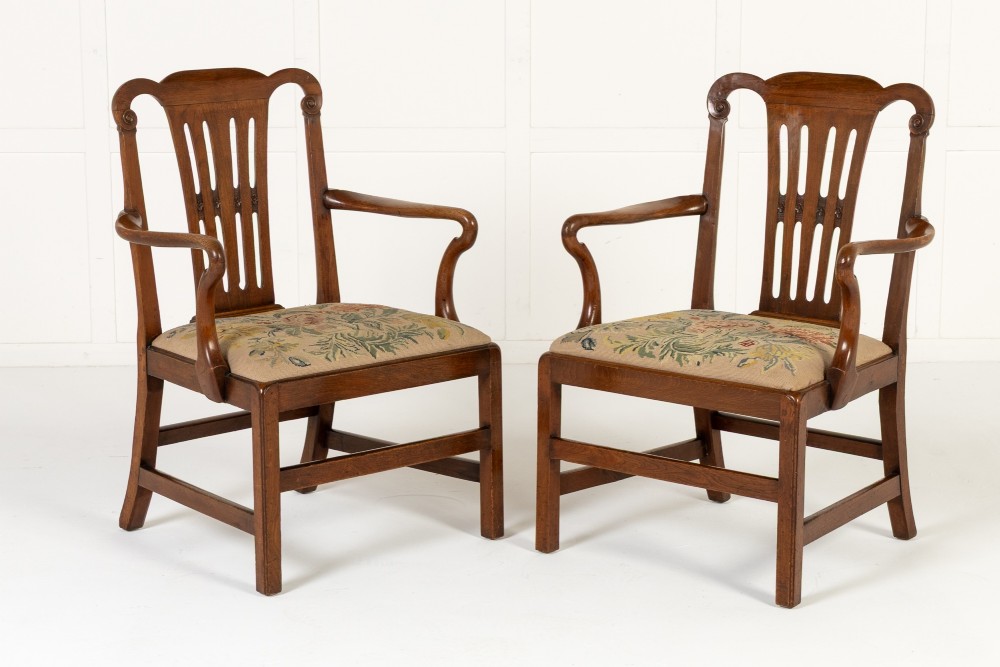 A pair of 18th-century George III mahogany armchairs featuring carved crest rails, vertical slatted splats, curved armrests, and needlepoint upholstered seats. View X