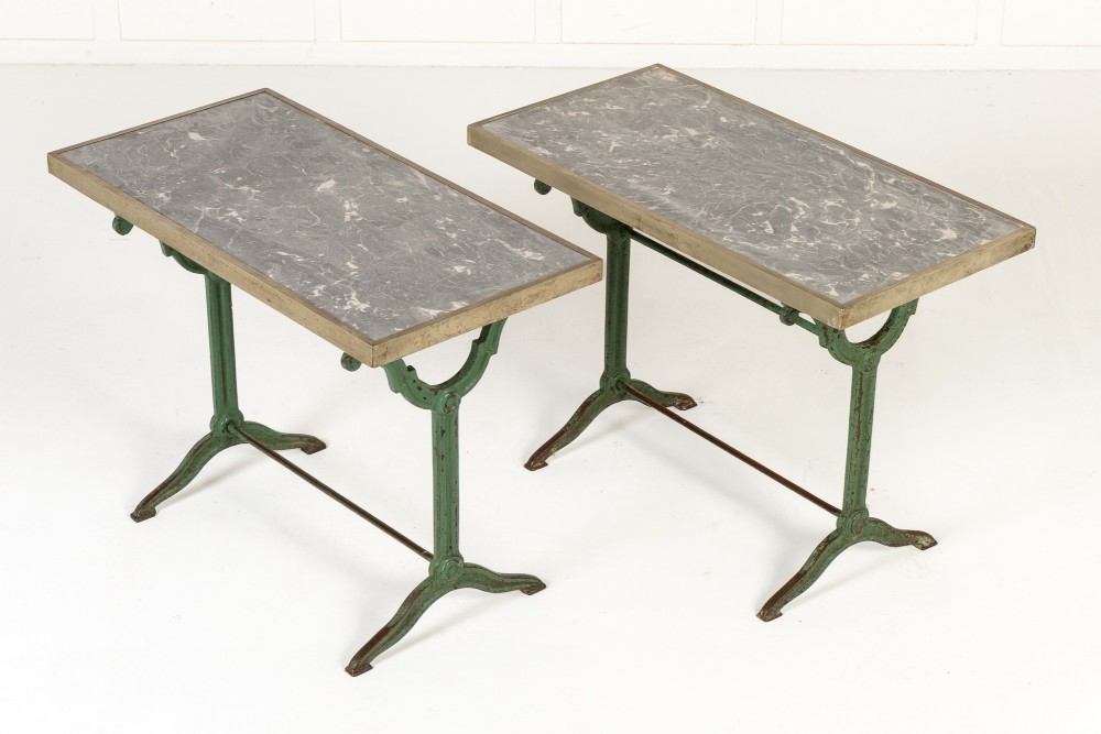 A pair of 19th-century bistro tables featuring rectangular grey veined marble tops framed in brass above weathered green-painted cast iron bases.