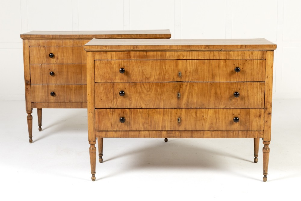 A pair of early 19th-century Italian cherrywood commodes featuring three full-width drawers with dark ebonised knobs and slender turned tapered legs.