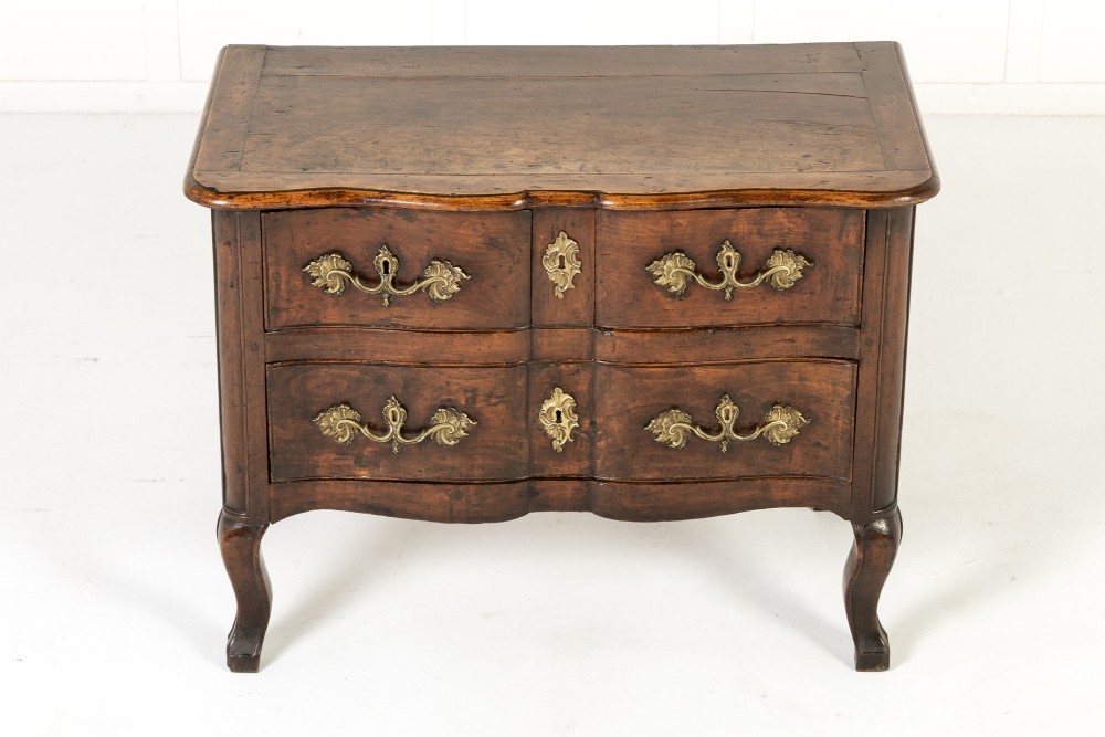 An 18th-century French walnut commode featuring two drawers with cast brass handles, a serpentine front, and cabriole legs.